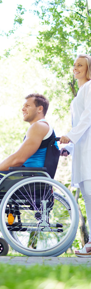 Pretty nurse walking with male patient in a wheelchair in park