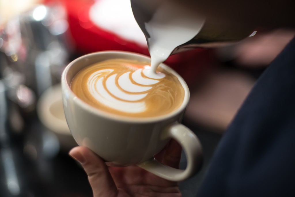 hand of barista making latte or cappuccino coffee pouring milk making latte art